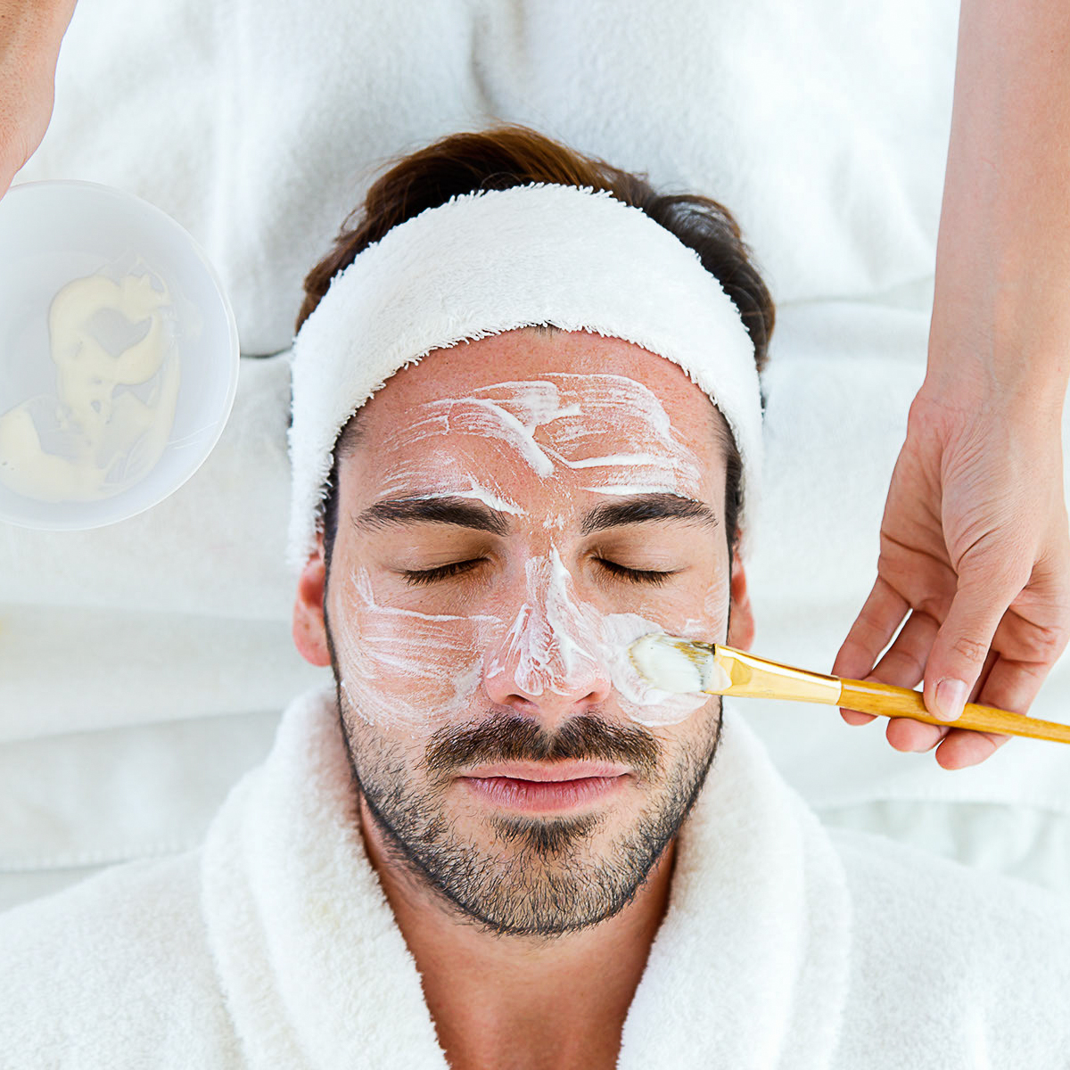 Man with clay facial mask in beauty spa.
